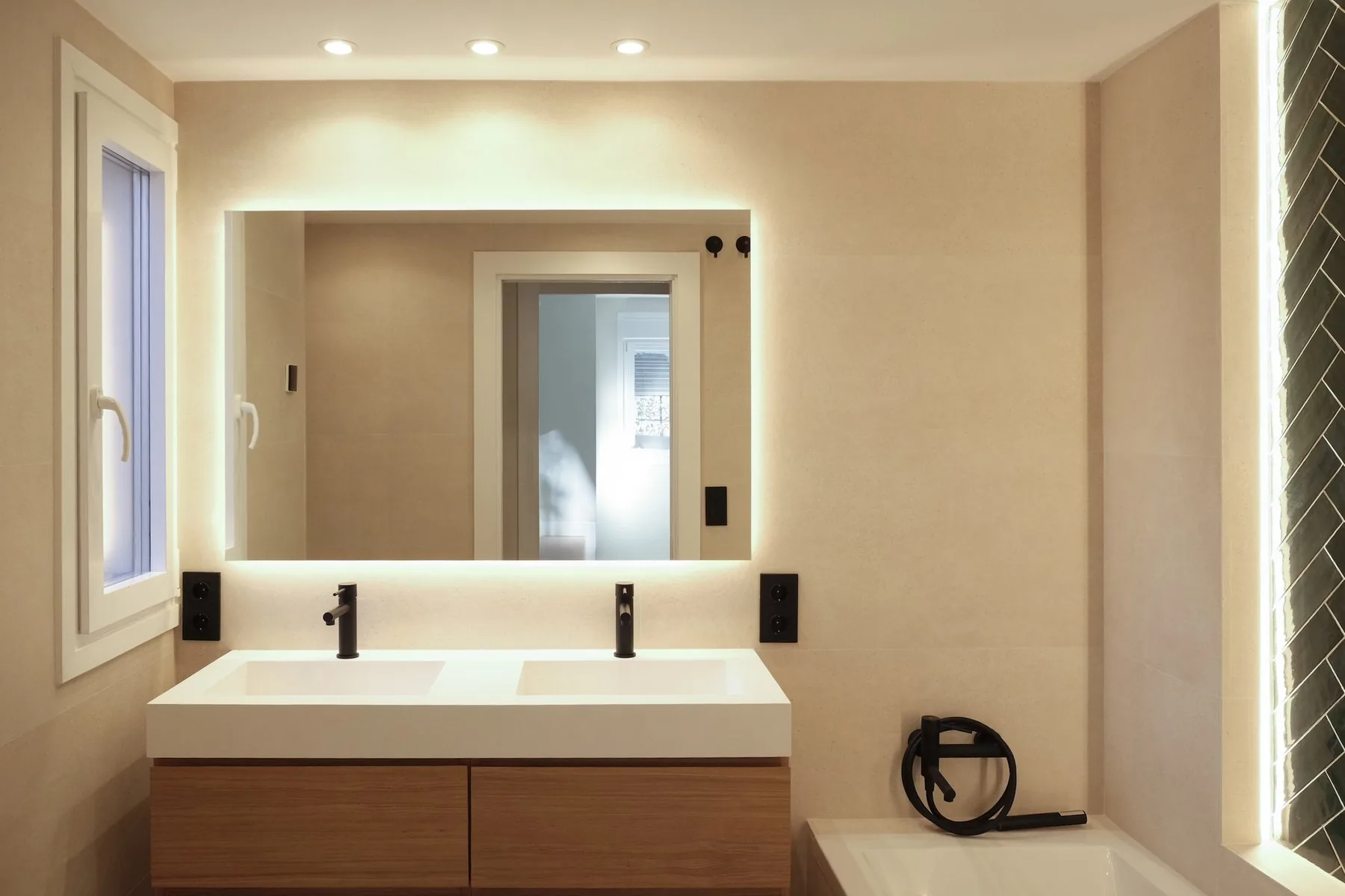 El baño principal, con el doble lavabo, el espejo retroiluminado y la bañera con la espiga verde oscuro al fondo