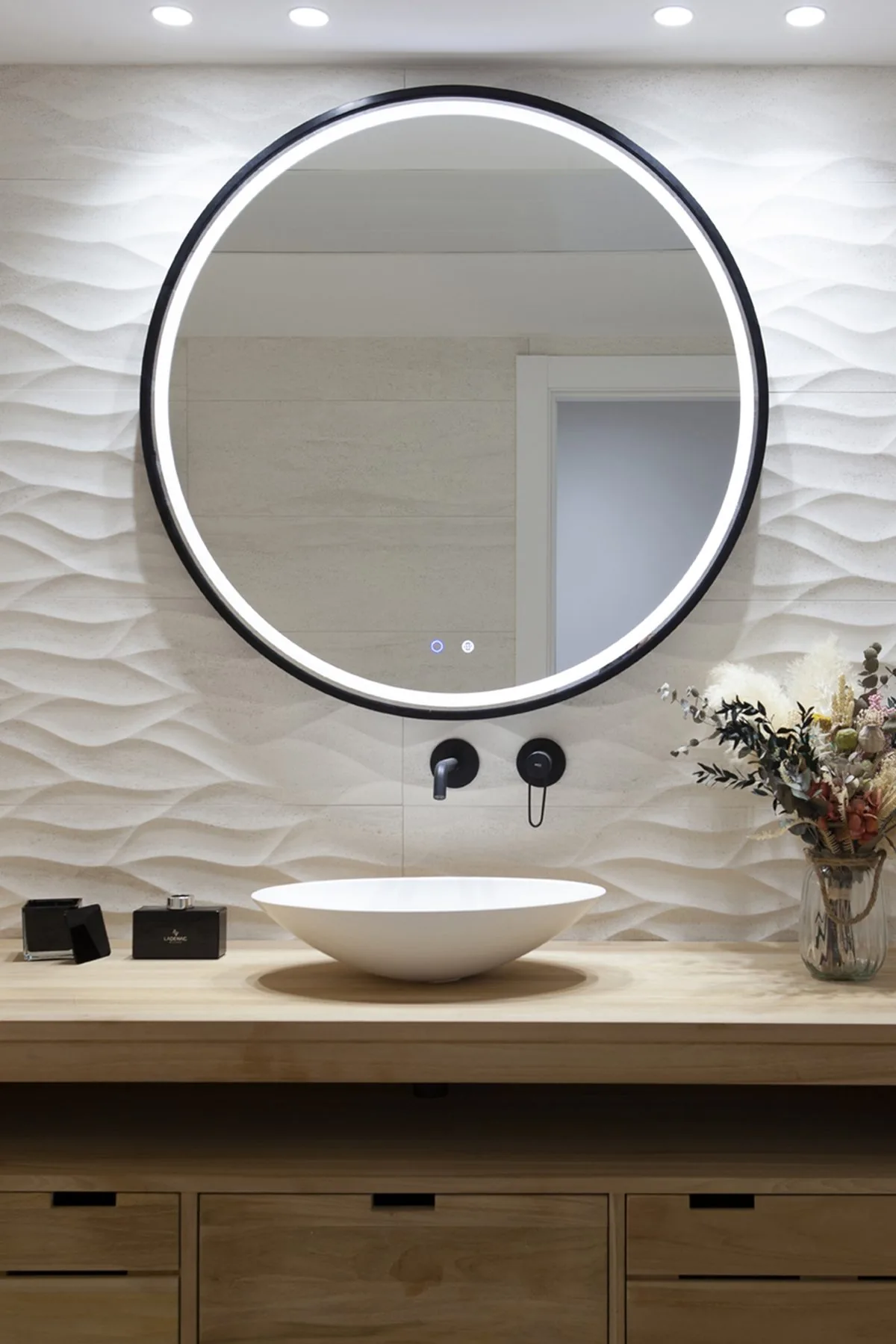 El baño de la bañera, con el espejo redondo retroiluminado sobre el mueble de madera