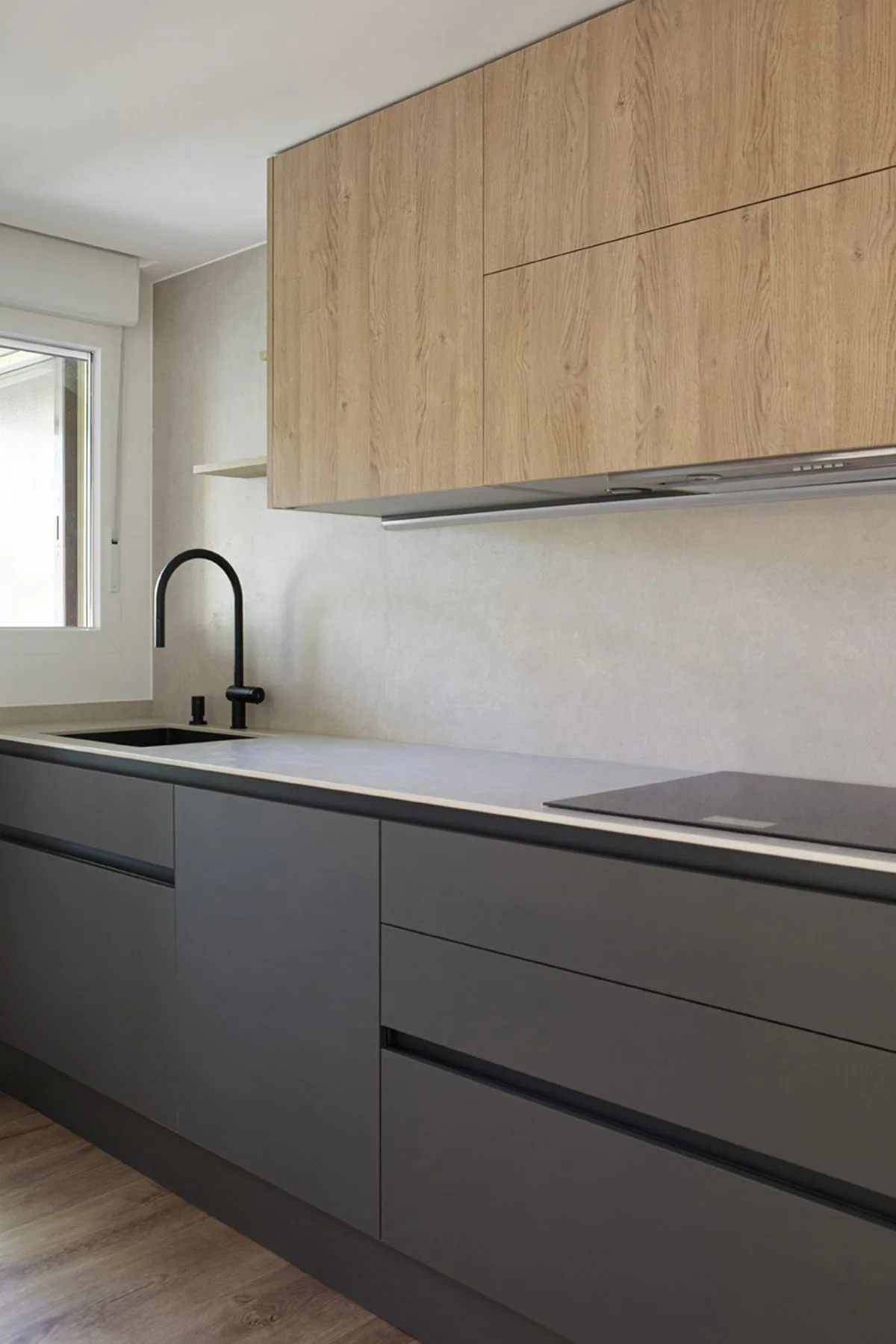 El frente de cocina en gris oscuro mate, con los módulos altos en tono madera — obra AGM9