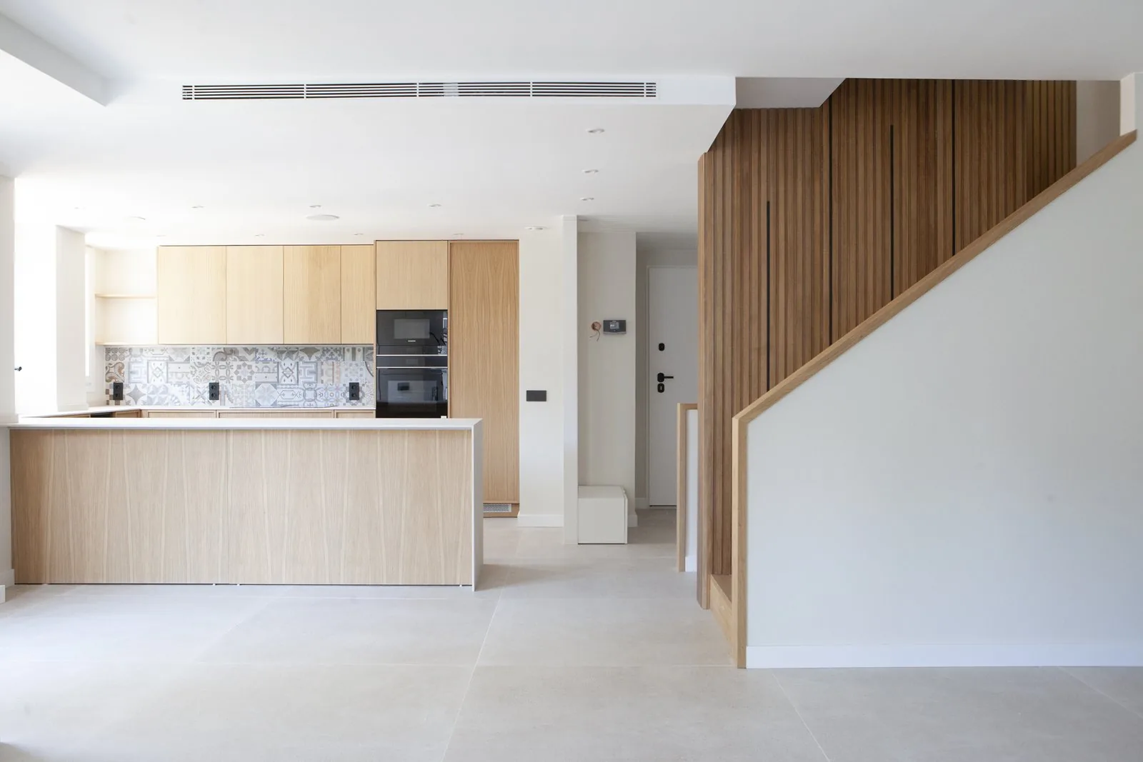 La zona de día del unifamiliar reformado: salón, cocina de roble y la escalera de listones al fondo