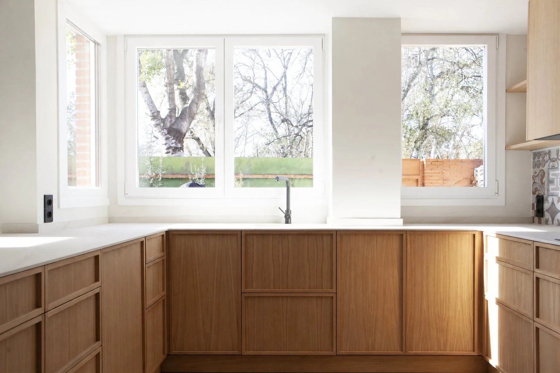 La península de la cocina se asoma a las ventanas en esquina, con el mueble en roble macizo y la grifería en negro