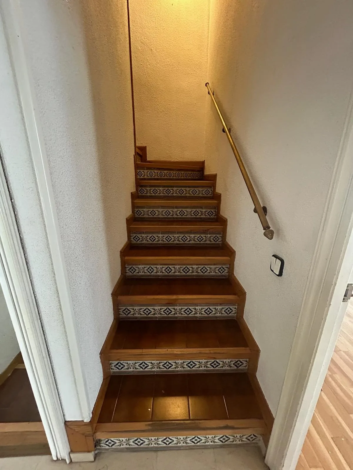 La escalera antigua, con las tabicas de azulejo y el pasamanos de madera