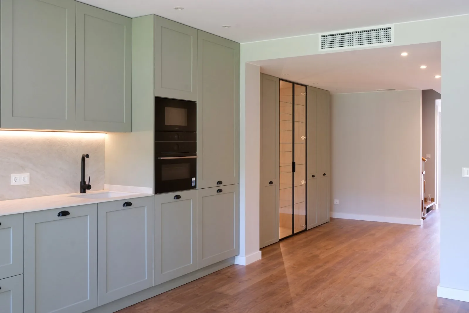 La cocina verde lacada a medida, con los tiradores negros y la vitrina de vidrio forrada de madera