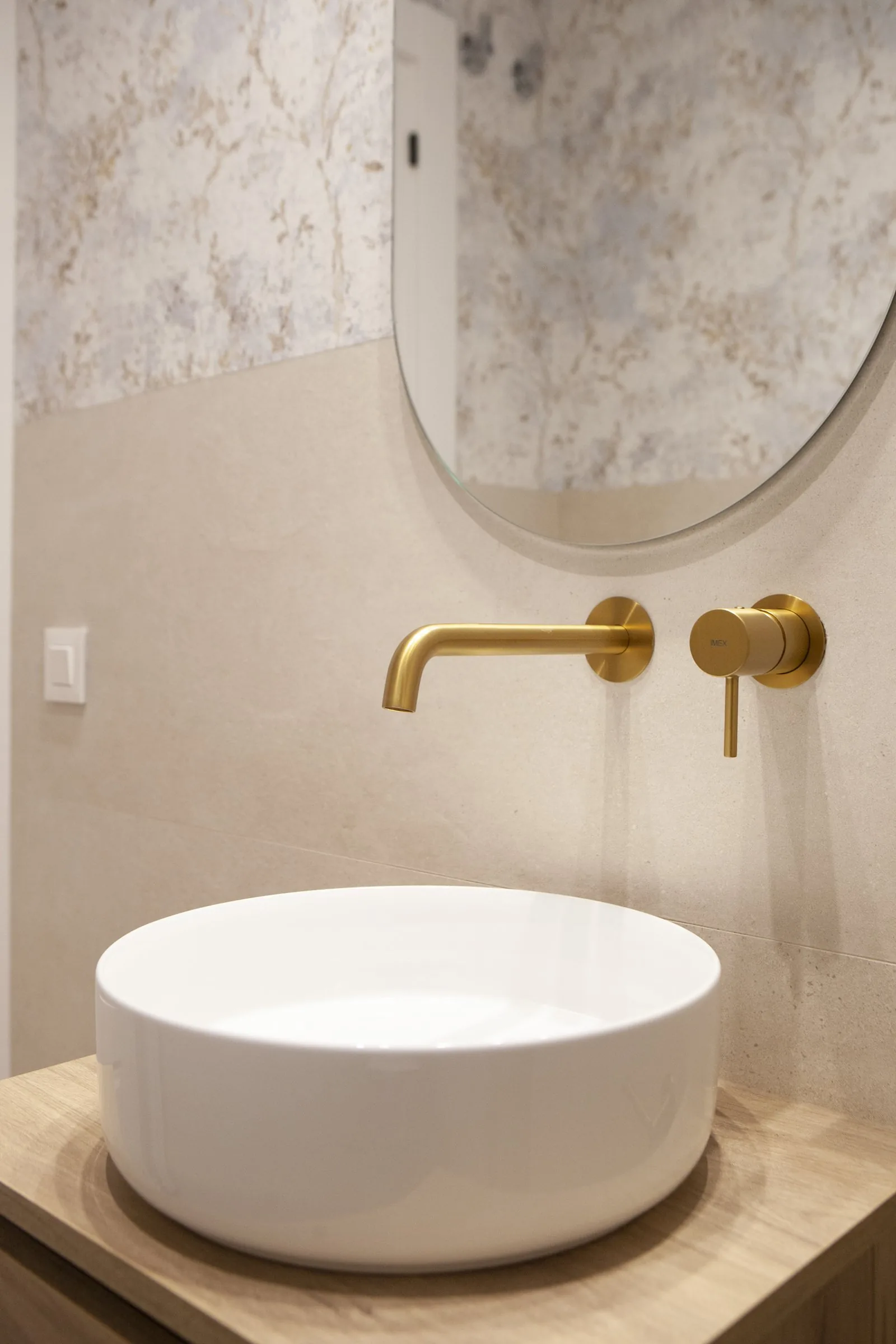 El lavabo redondo sobre mueble a medida, con grifería dorada y papel pintado