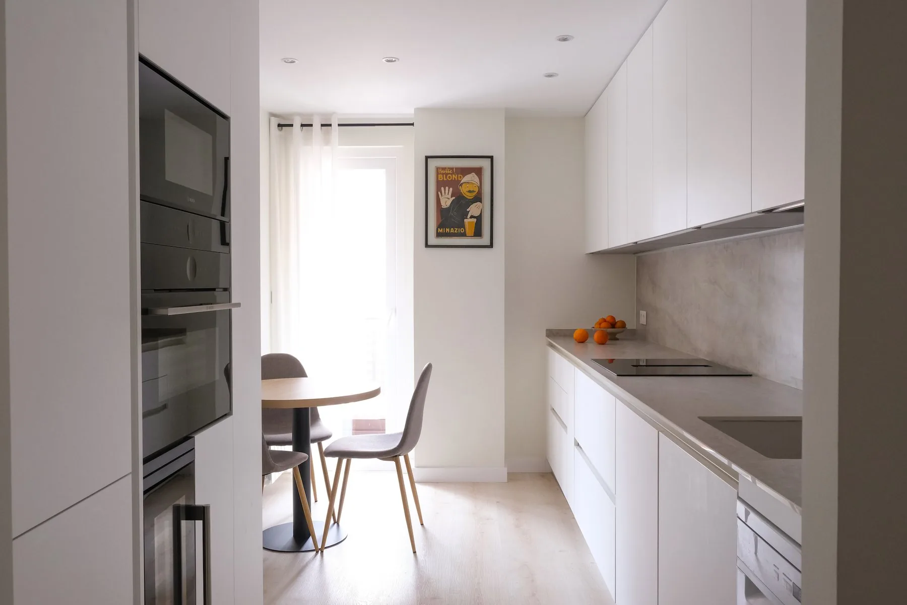 La cocina terminada, con el frente claro y la mesa de desayuno junto a la ventana — obra EPB23