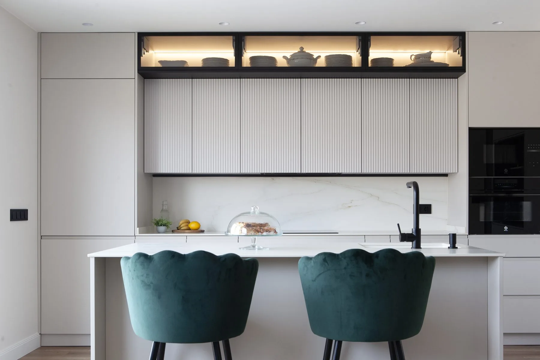 El frente completo de la cocina, con la isla, los muebles altos ranurados y las vitrinas iluminadas