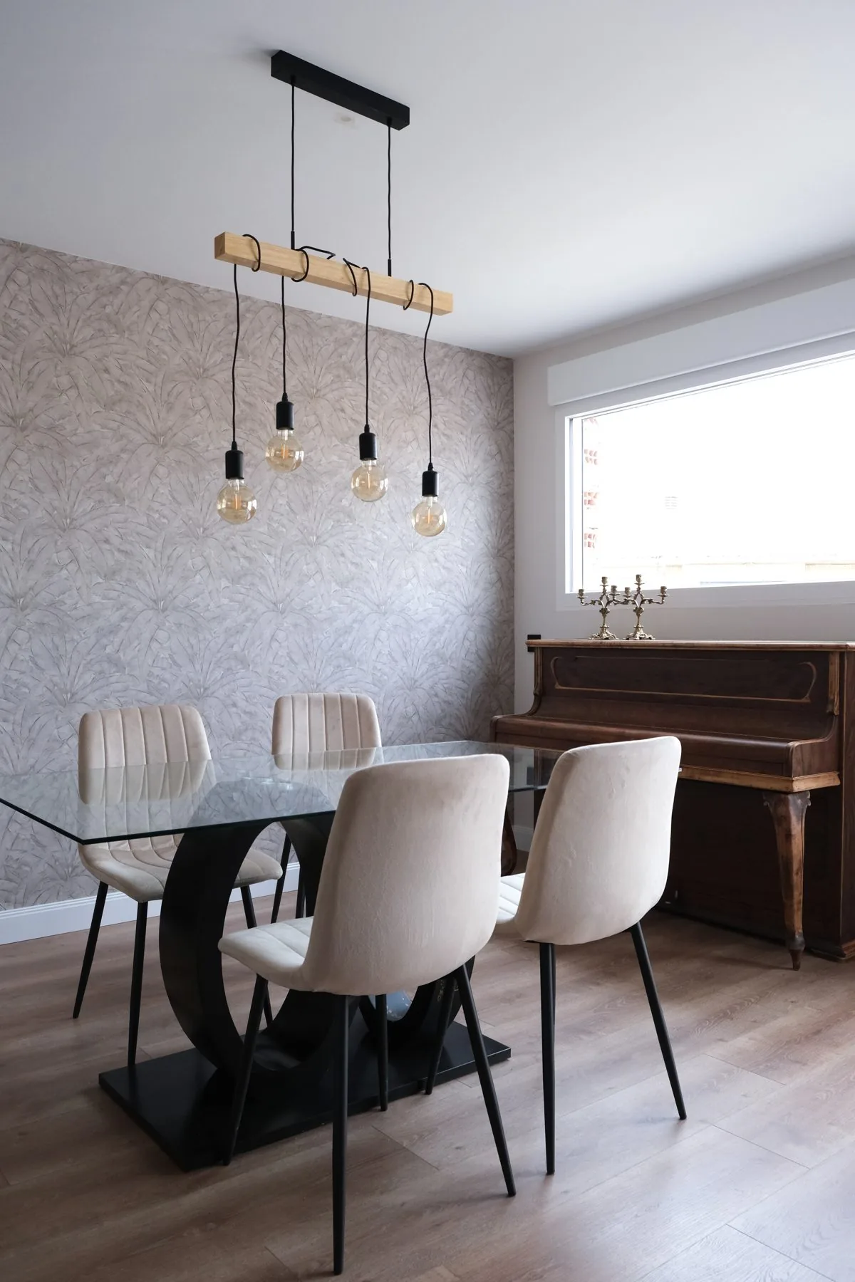 El comedor, con la mesa de cristal, el papel pintado vegetal y el piano de pared