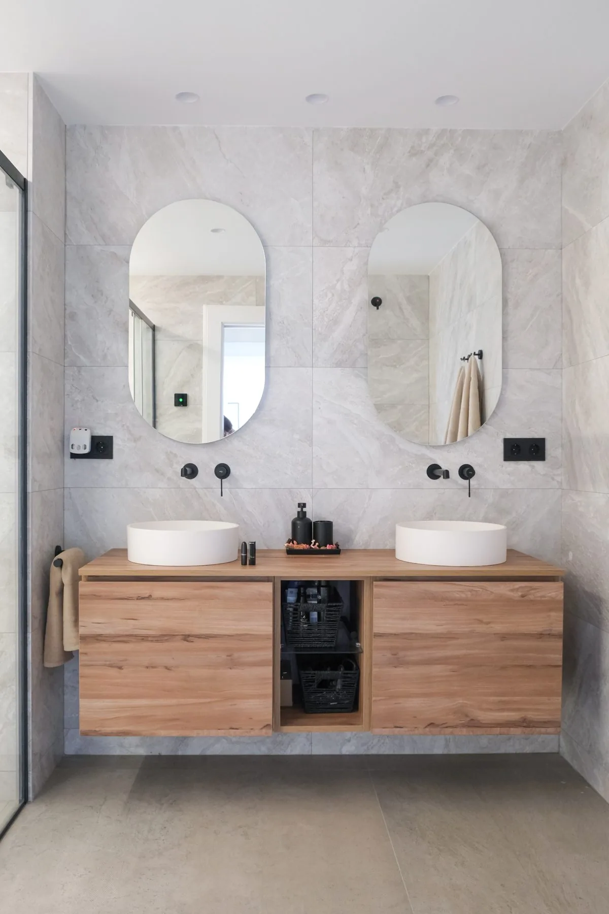 Baño suite: doble lavabo sobre encimera de madera con dos espejos ovalados y grifería negra