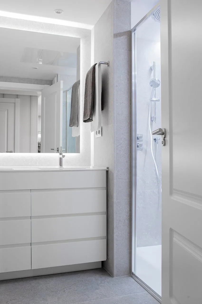 El mueble blanco de cajones del baño general, con la ducha al fondo