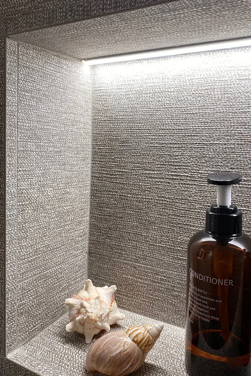 La hornacina retroiluminada del baño suite, con la luz rasante sobre la trama del porcelánico — obra JZ14