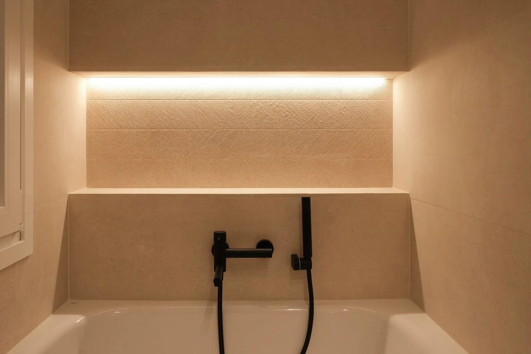Baño general: la bañera bajo la hornacina con luz indirecta y la grifería negra