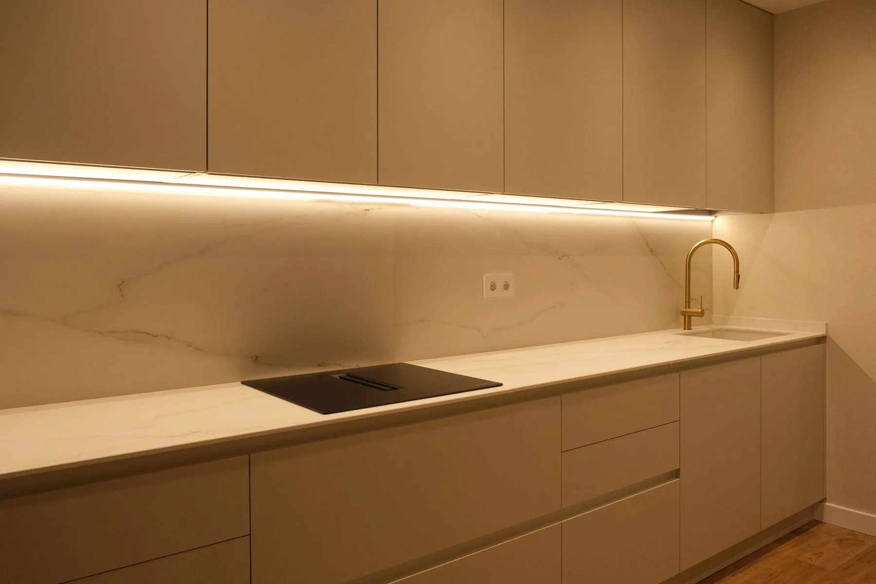El frente completo de la cocina, con la placa y el fregadero bajo la iluminación de los muebles altos
