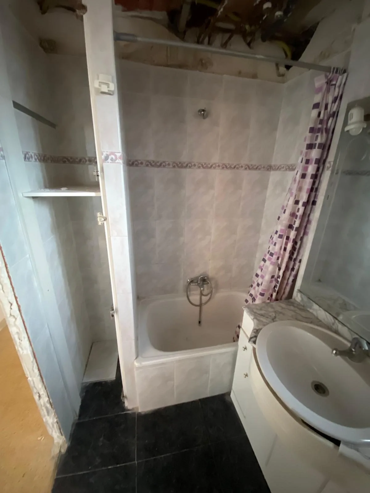 El baño antes de la obra, con la bañera, el suelo oscuro y el lavabo integrado en el mueble curvo