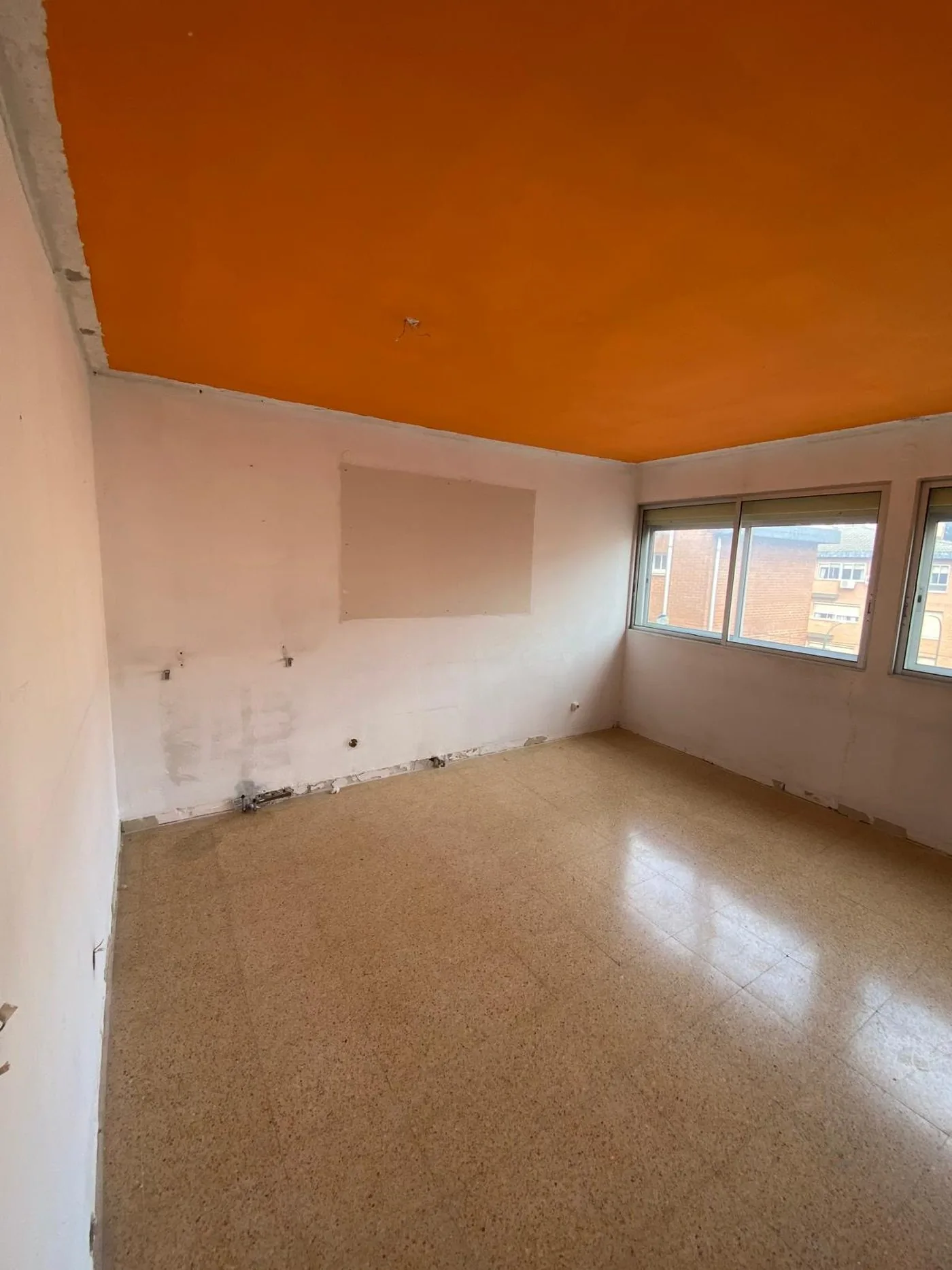 Una de las habitaciones antes de la obra, vacía, con el techo naranja y el suelo de terrazo