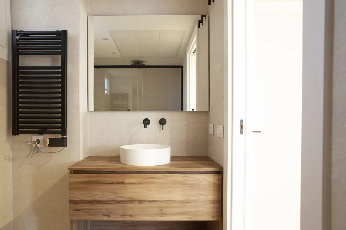 El baño desde la puerta: el mueble de madera, el lavabo redondo y el espejo retroiluminado