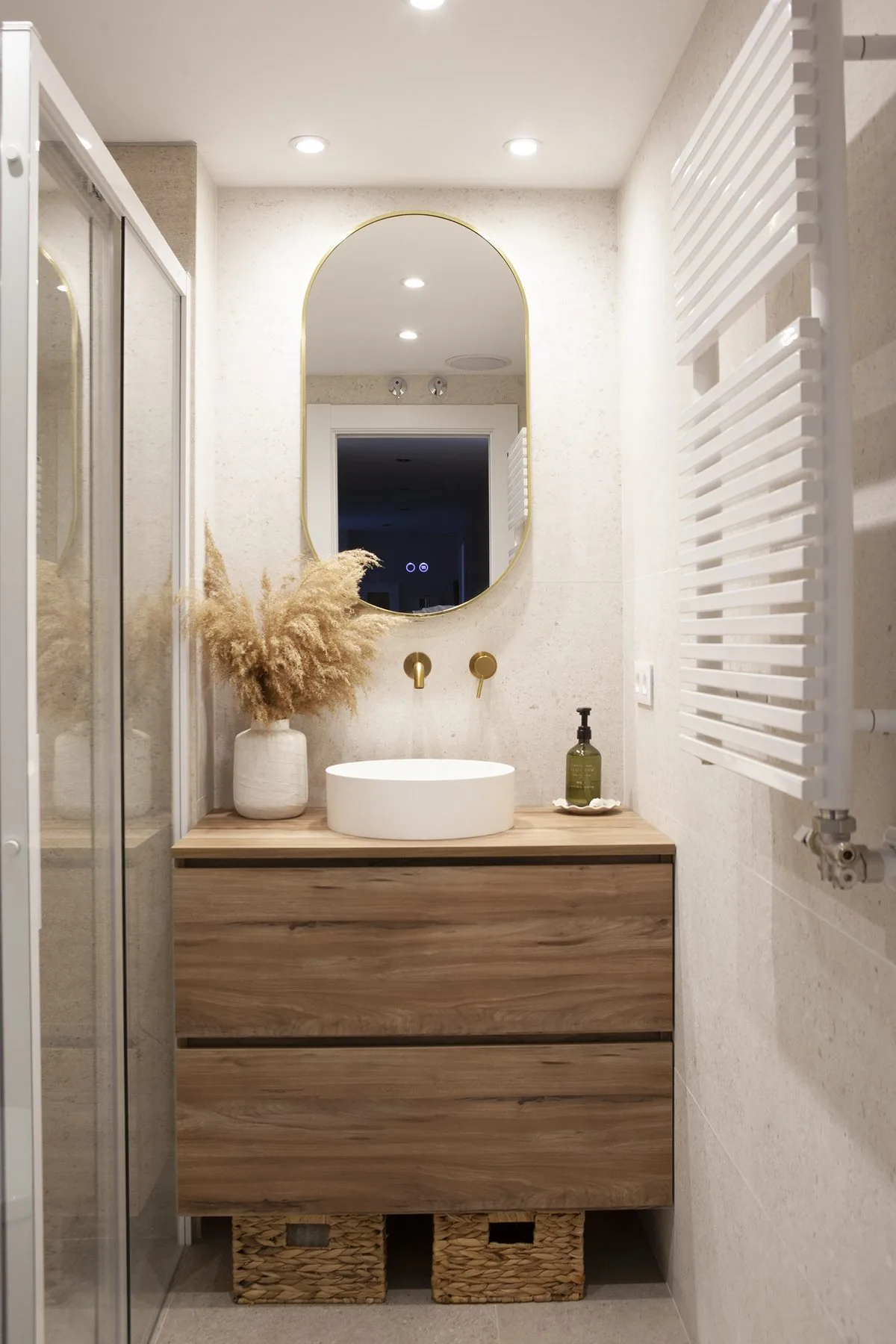 El baño hoy desde la puerta: el mueble de madera con las cestas, el lavabo redondo y el espejo ovalado retroiluminado