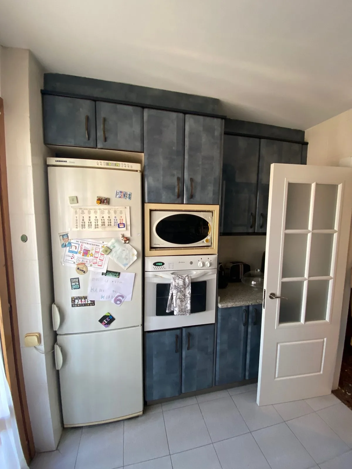 El mismo testero antes de la obra, con los muebles de laca azul, el frigorífico y la puerta de cuarterones a la derecha