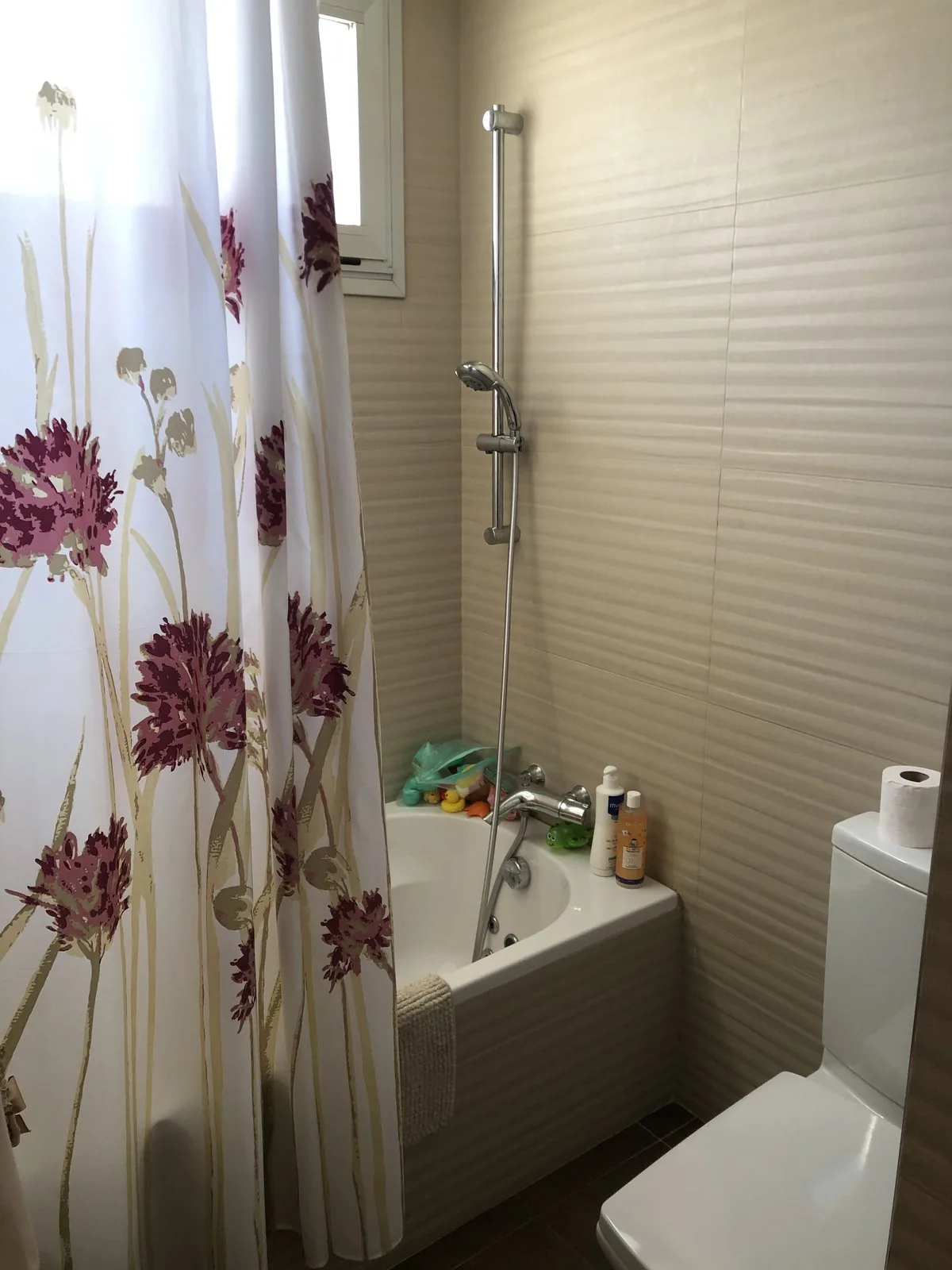 El baño de la primera planta antes de la obra, con la bañera, la mampara textil de flores y el alicatado claro
