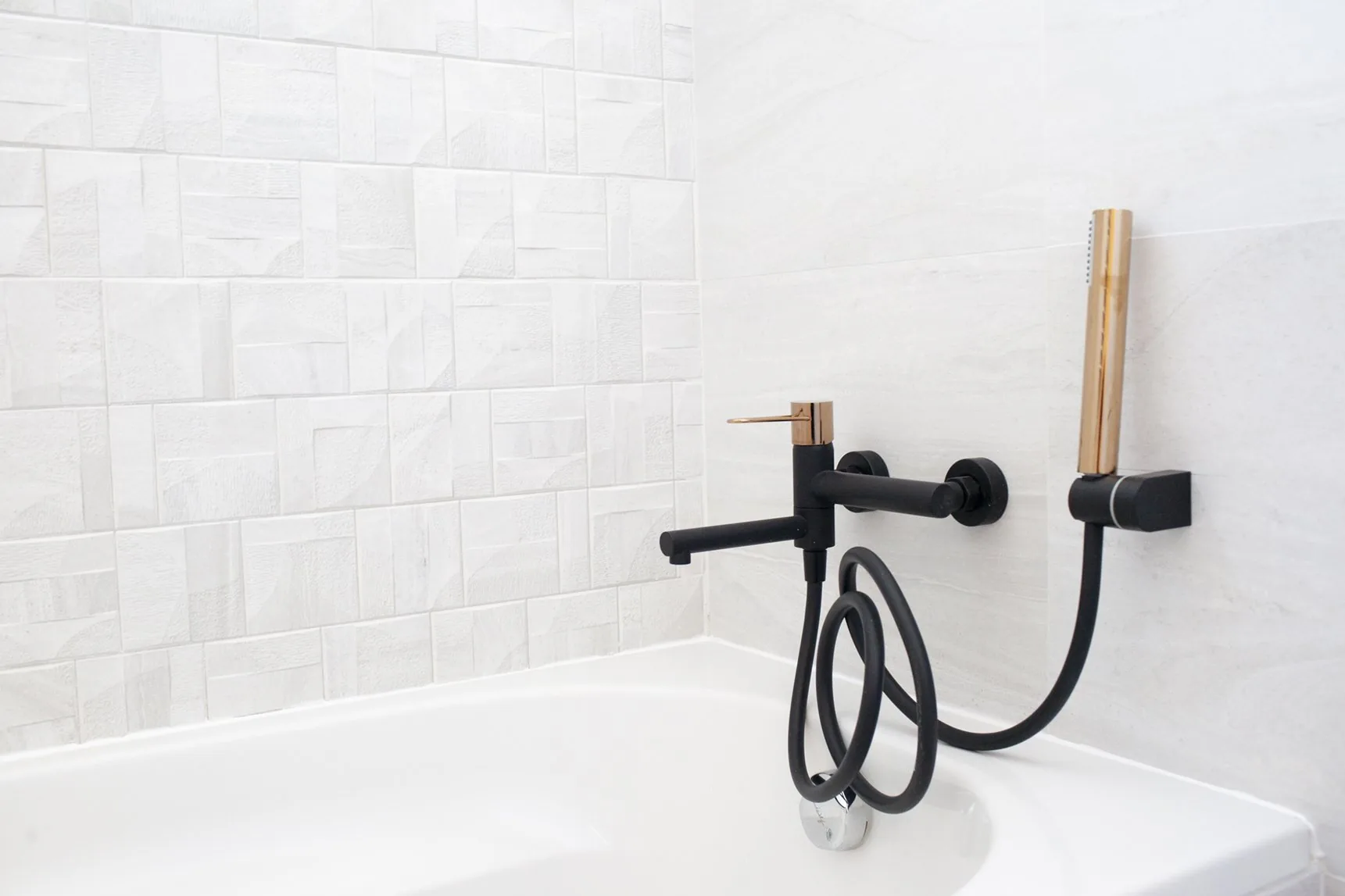 La bañera del baño de la primera planta, con la grifería empotrada de pared en negro y latón sobre el azulejo blanco de relieve