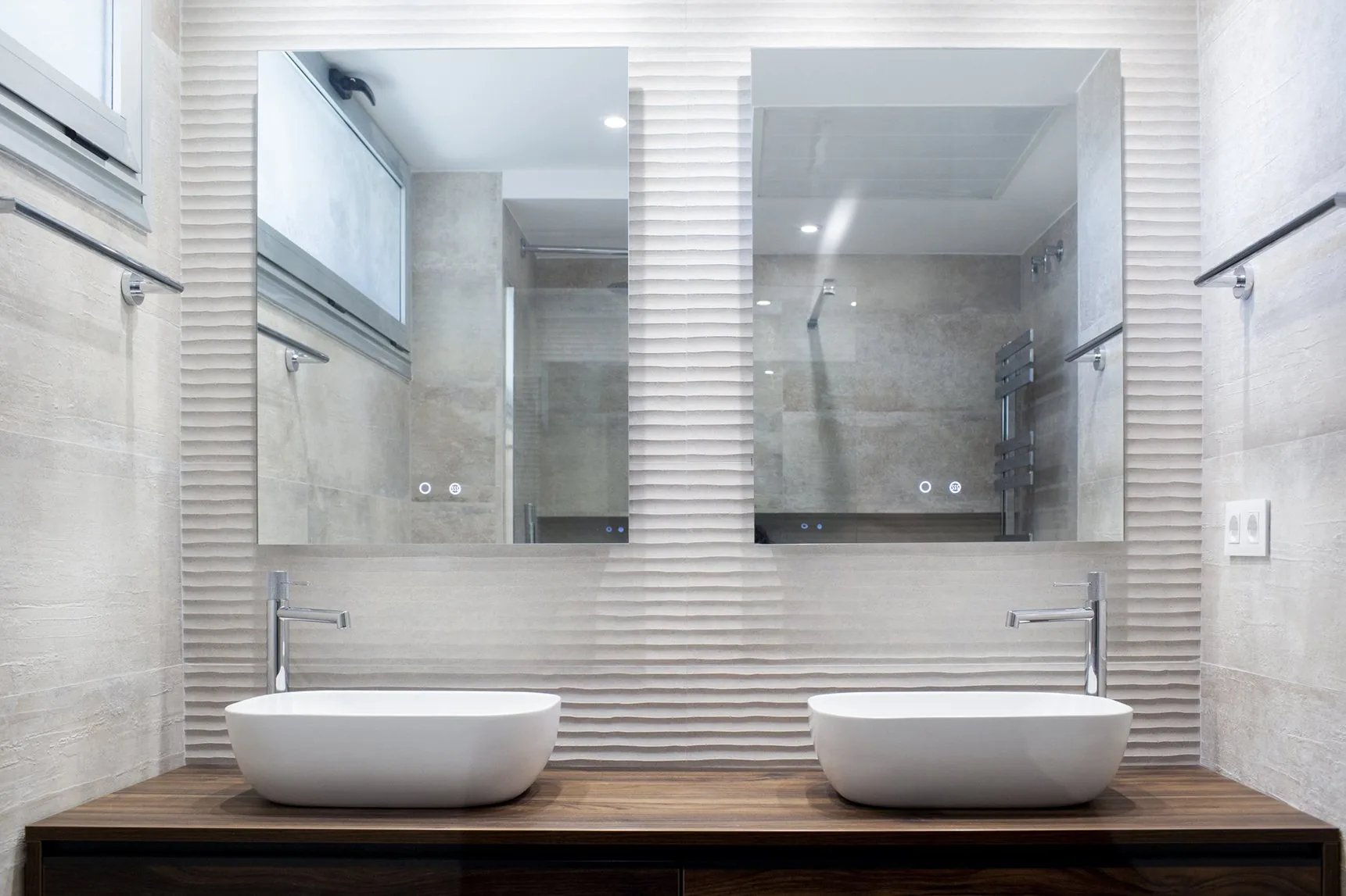 El doble lavabo del baño de la planta baja sobre la encimera de nogal, bajo el espejo retroiluminado