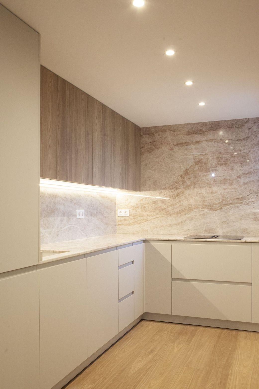Reforma cocina baño Zaragoza: cocina en U con pared de piedra natural de vetas rosadas, muebles altos en acabado roble y frentes blancos
