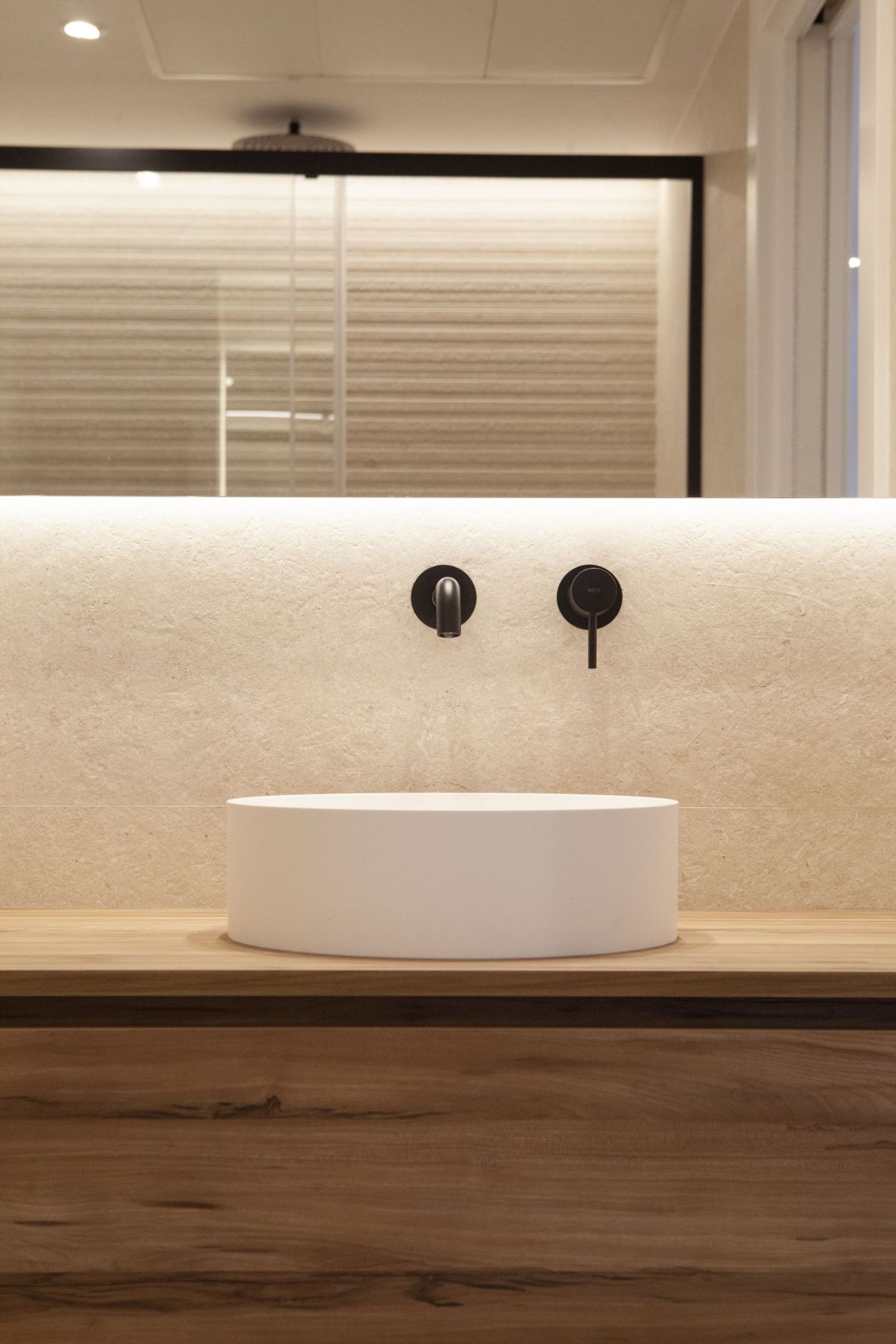 Lavabo sobre encimera frontal con griferia negra empotrada y reflejo de la ducha en el espejo