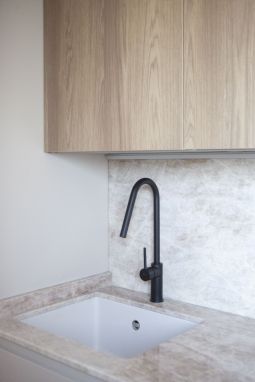 Fregadero con grifería negra mate bajo ventana lateral, mueble alto de madera acabado roble y encimera de piedra natural