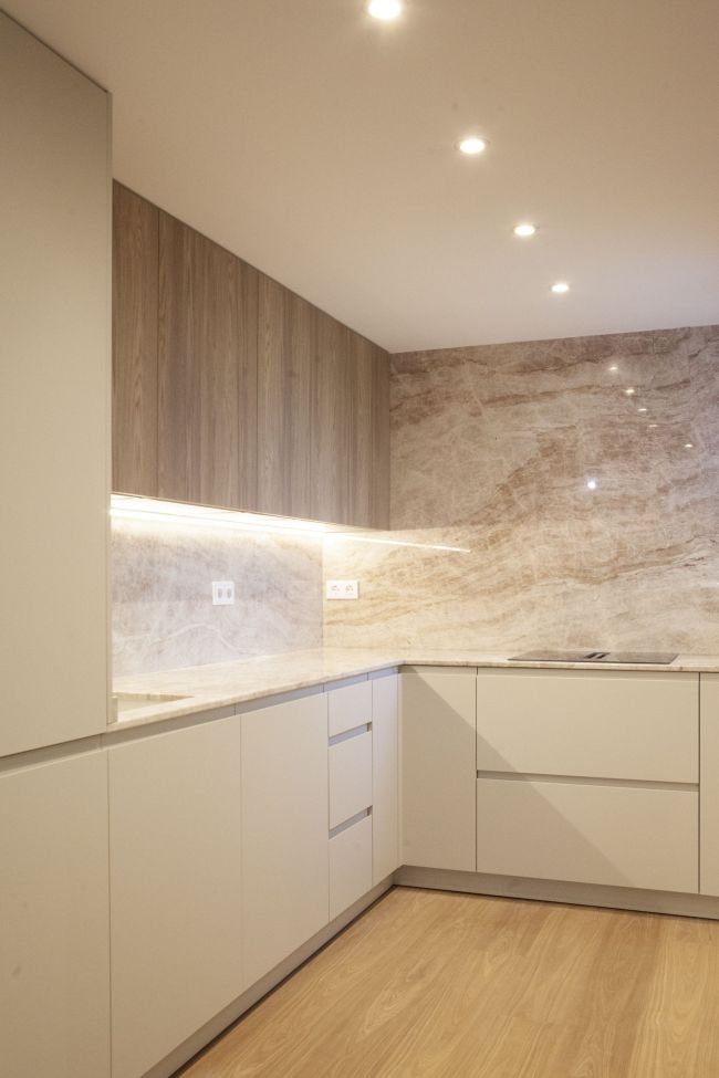 Reforma cocina baño Zaragoza: cocina en U con pared de piedra natural de vetas rosadas, muebles altos en acabado roble y frentes blancos